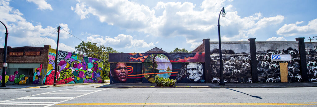 Color photograph showing storefronts painted with bright murals depicting historical figures and abstract imagery.
