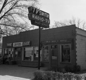 Black and white photogrpah of a brick storefront with a high sign above it with the words TV Smith Radio-TV Sales Services in large offset letters.