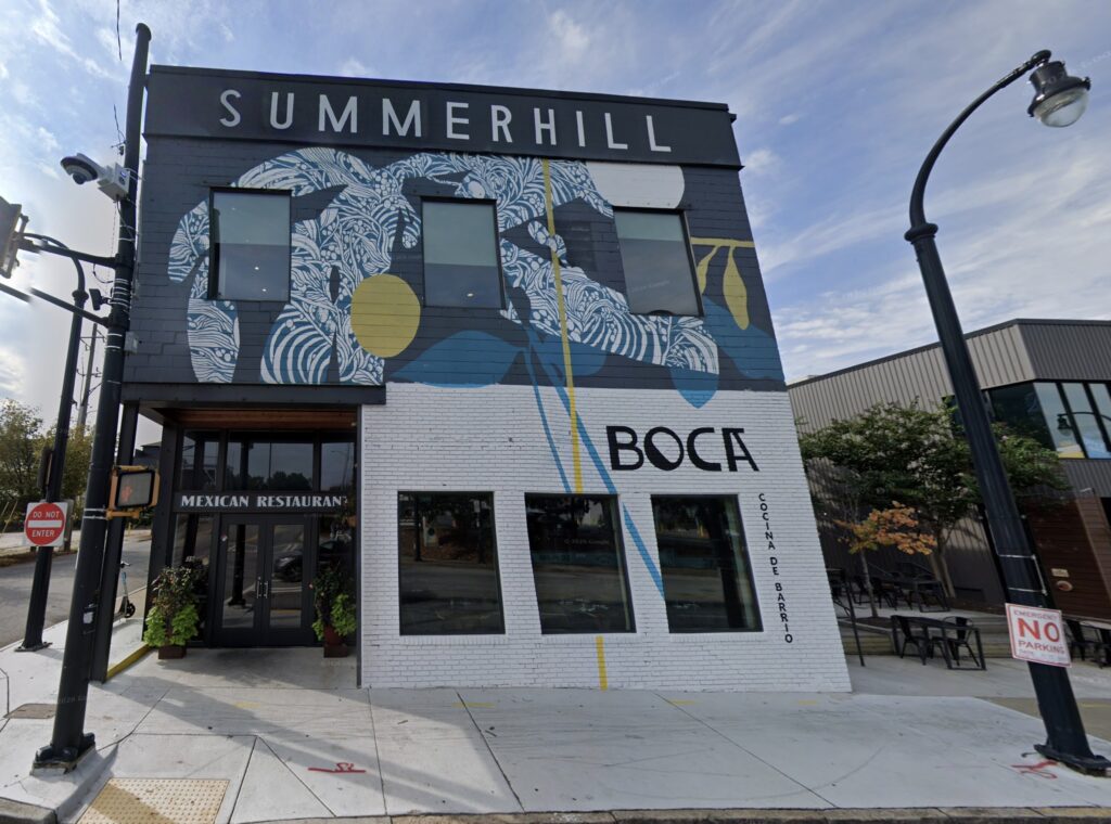 Color photograph of two-story storefront with mural painted on the front with the word "Summerhill" at the top above a design in blue and yellow around three windows. Below, three more windows stand beside a glass doorway.
