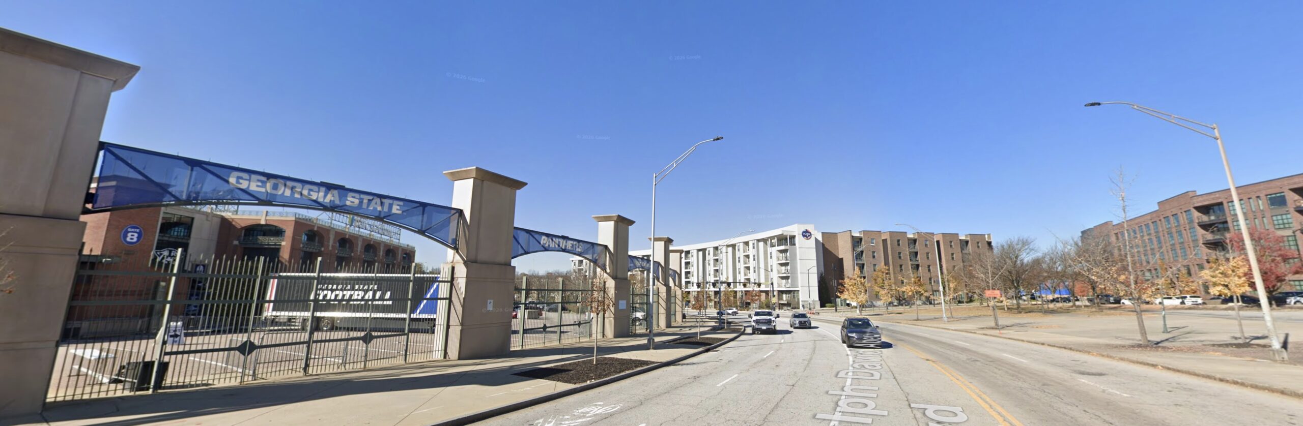 Georgia State University stadium gate dominates the left side of an image showing a road with cars driving from the background to the foreground.
