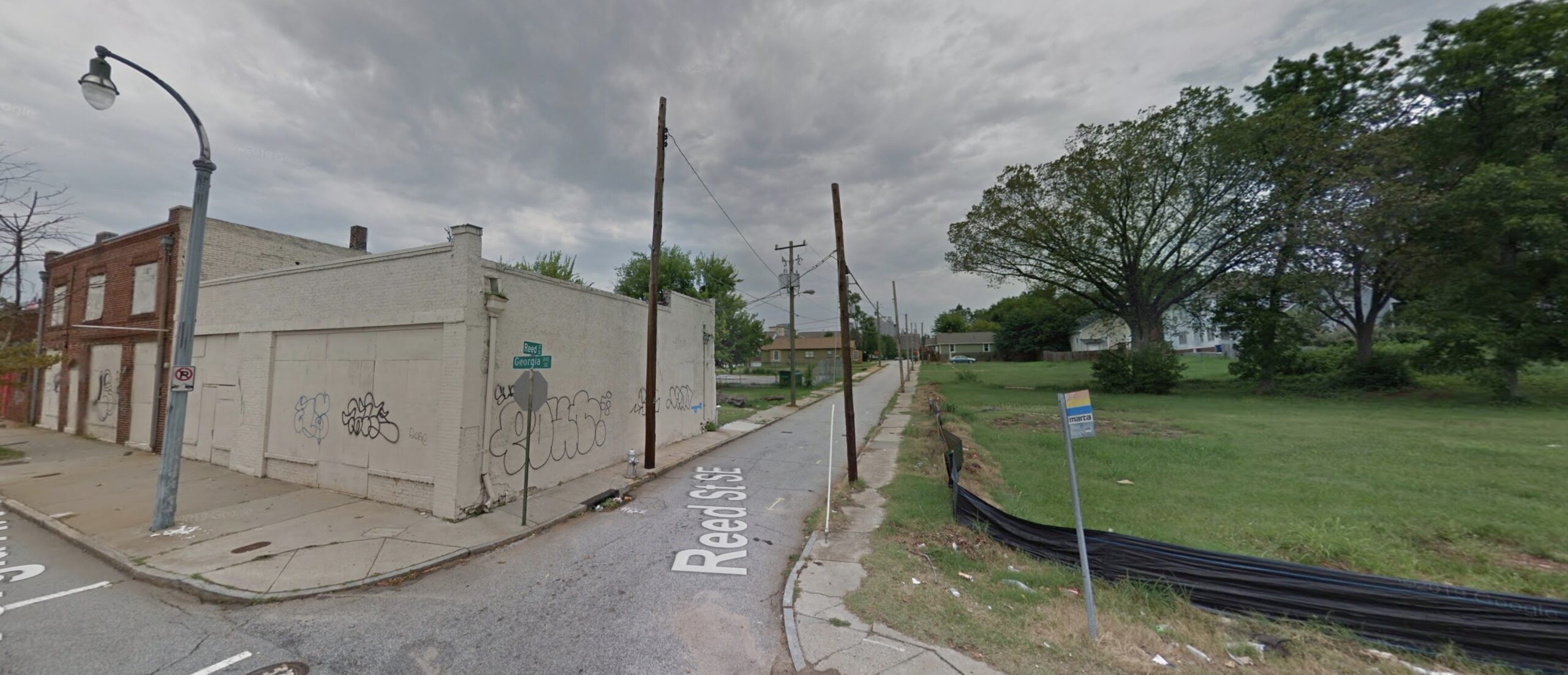 Color photo of a street corner with empty storefronts, boarded up, with graffiti on them. 