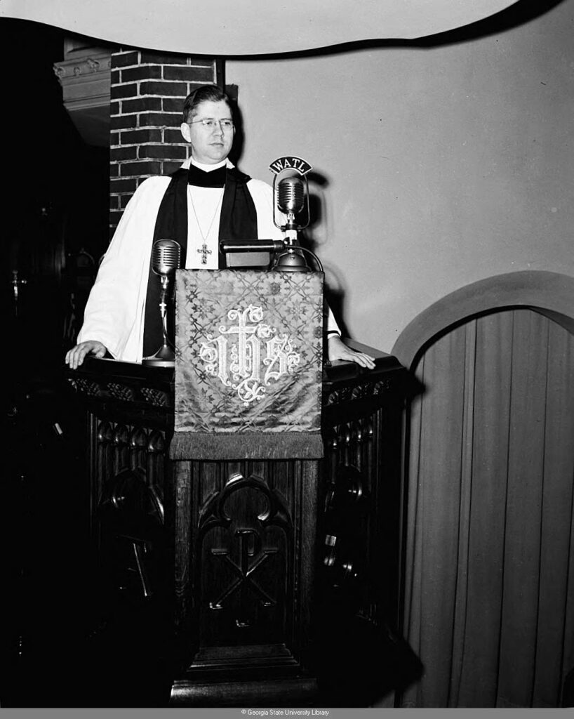 black and white image of a priest at the pulpit with a WATL radio microphone in front of him