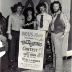 black and white image of three men and one woman holding a sign that reads WGUS Radio will present a... Taco Eating Contest here at Taco VIva 