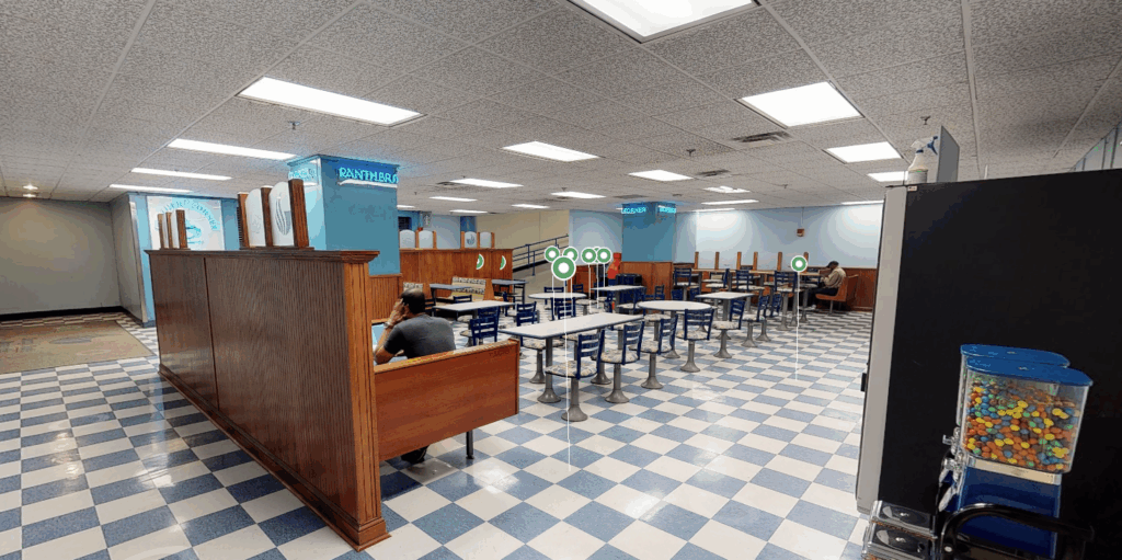 Color image of a cafe space with booths and tables and blue and white linoleum floor. Green circles indicate that the image is a still from a Matterport rendering